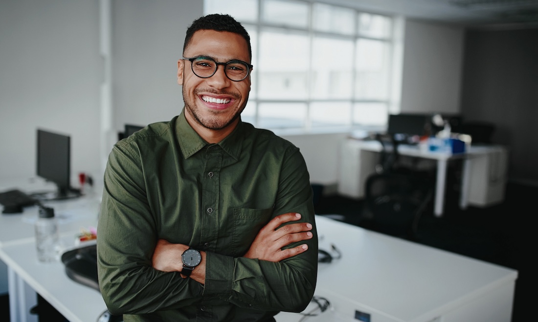 Portrait of a happy confident young african american businessman standing with his arms crossed looking at camera