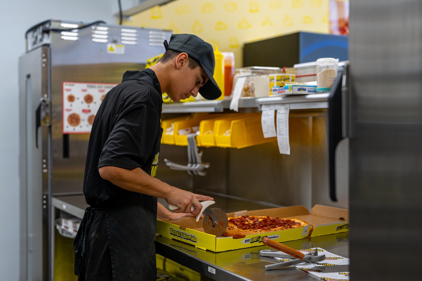 A hungry howie’s employee slicing a pizza in the kitchen A hungry howie's employee slicing a pizza in the kitchen