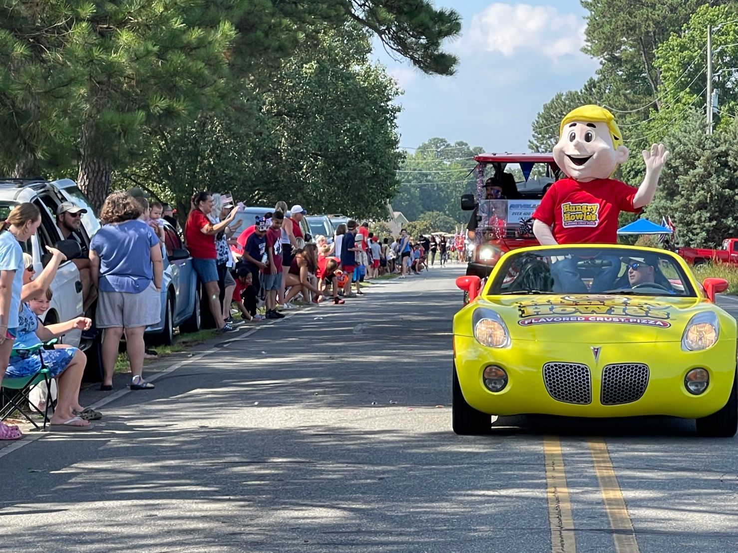 Hungry Howie's Mascot in a yellow car parading downtown with onlookers waving