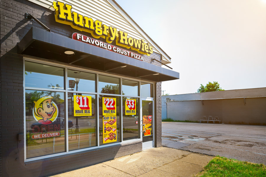Exterior storefront of a Hungry Howie's Flavored Crust Pizza restaurant with promotional deal signs in the windows.